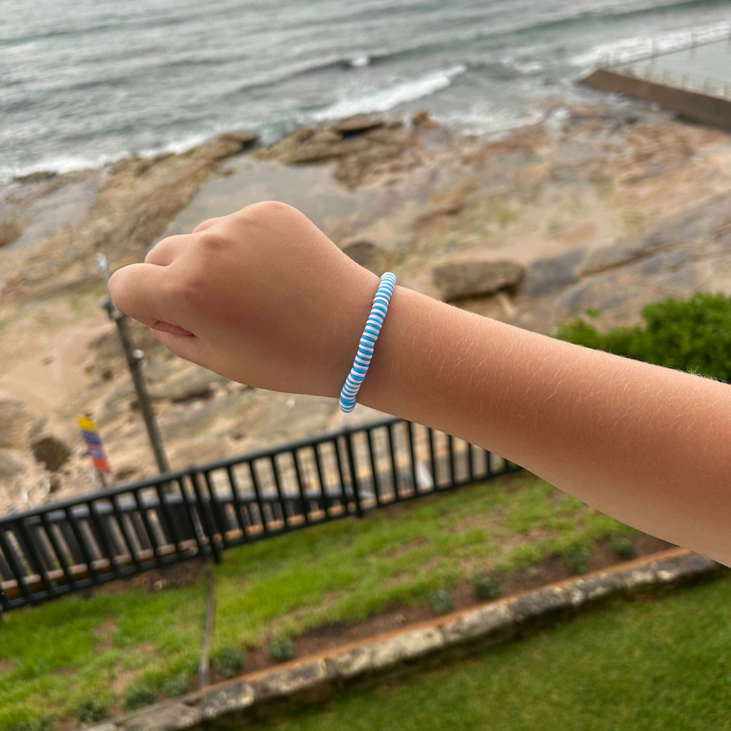 Blue and white bracelet worn on a child’s wrist with an ocean background