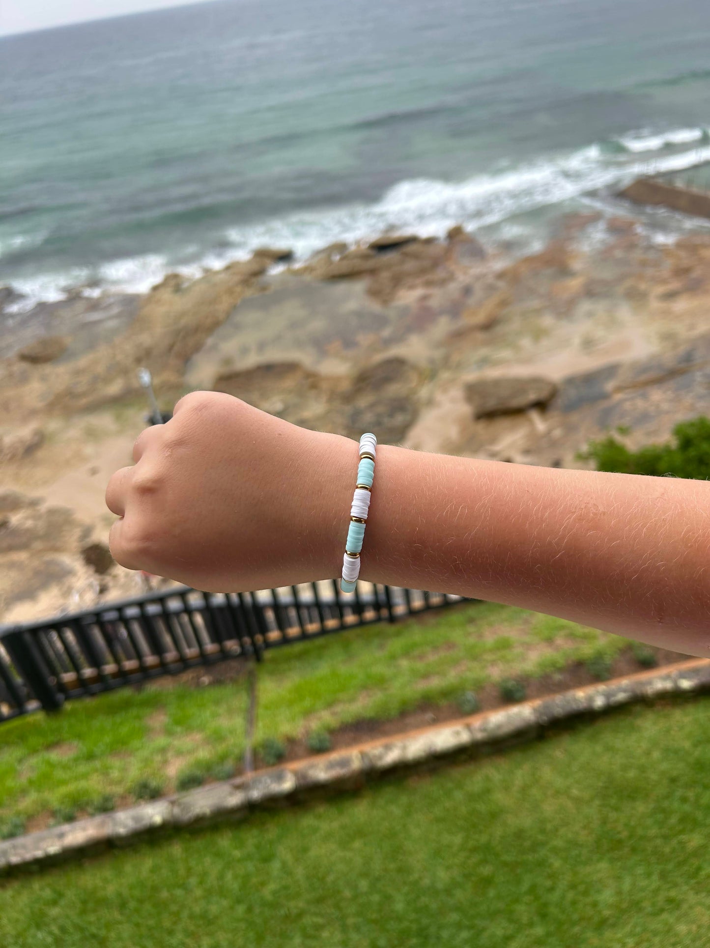 Blue and white bracelet with gold spacers worn on a child’s wrist with an ocean background