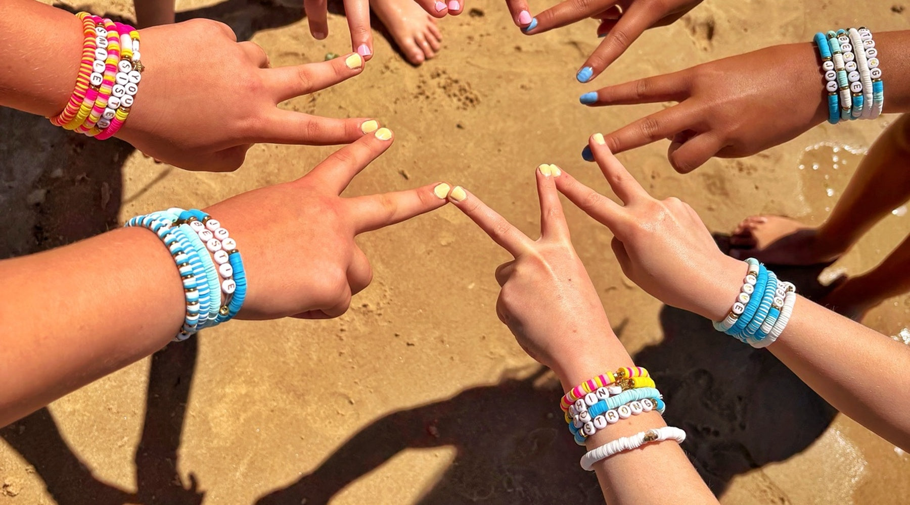 Hands with colorful bracelets making peace signs on a sandy background